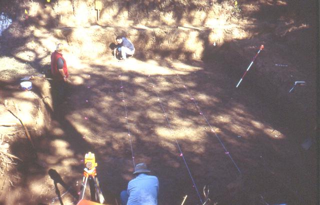 Two people using string to lay out grid lines at excavation site while a third person watches