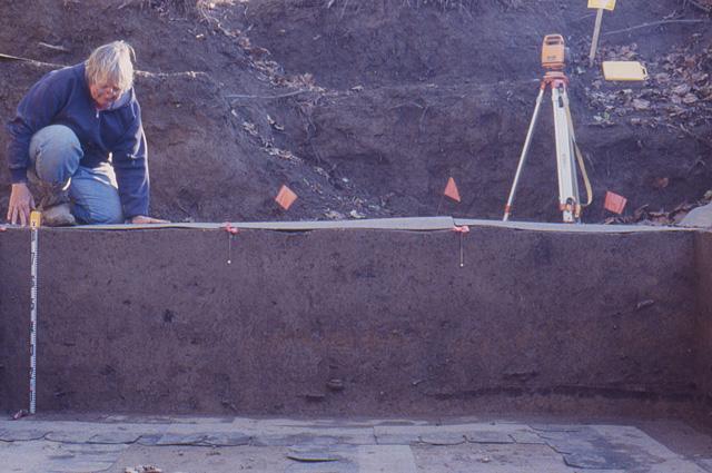 a person nealing by the excavation using a measuring tape to measure the depth
