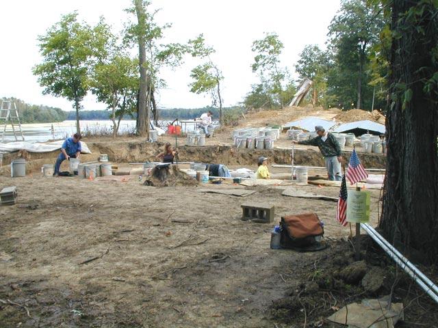 Two American flags in the foreground while 5 people are working the excavation site