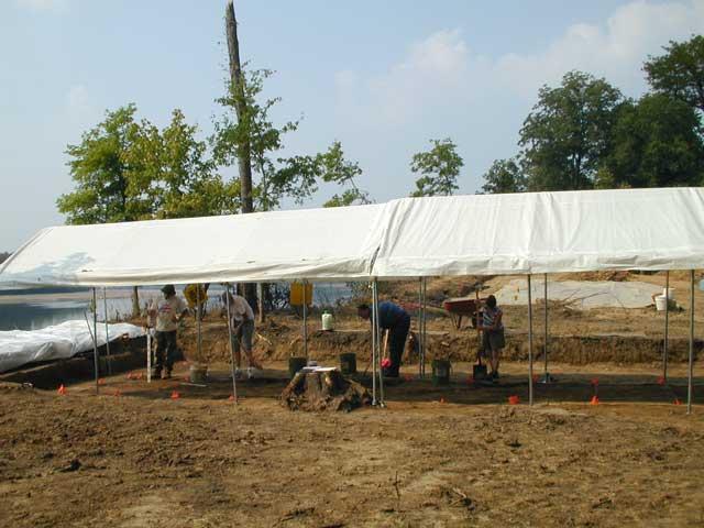 Two canopies cover the excavation area, while 4 people work under them.