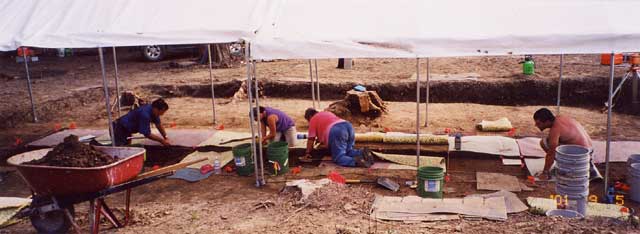 Four people working site under canopy