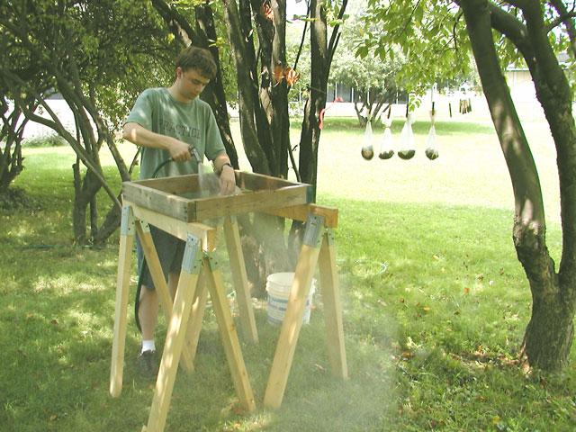 Sean O'Brian uses a hose to wash the dissolved soil from the artifacts and natural and cultural residues inside the bag. (Four bags of cultural material hang on a line to dry.)